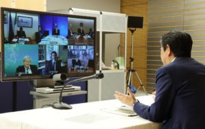 A speaker siting in front of the camera, on a video conference. In fron t of him a Zoom screen with 6 other participants on a video conference call.
